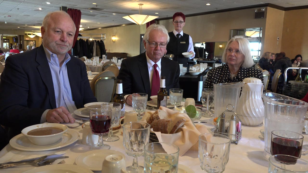 In Chicago, Illinois, the table remains filled with glasses, soup, bread, pitchers, and seated adults while a server stands near the back of the group.