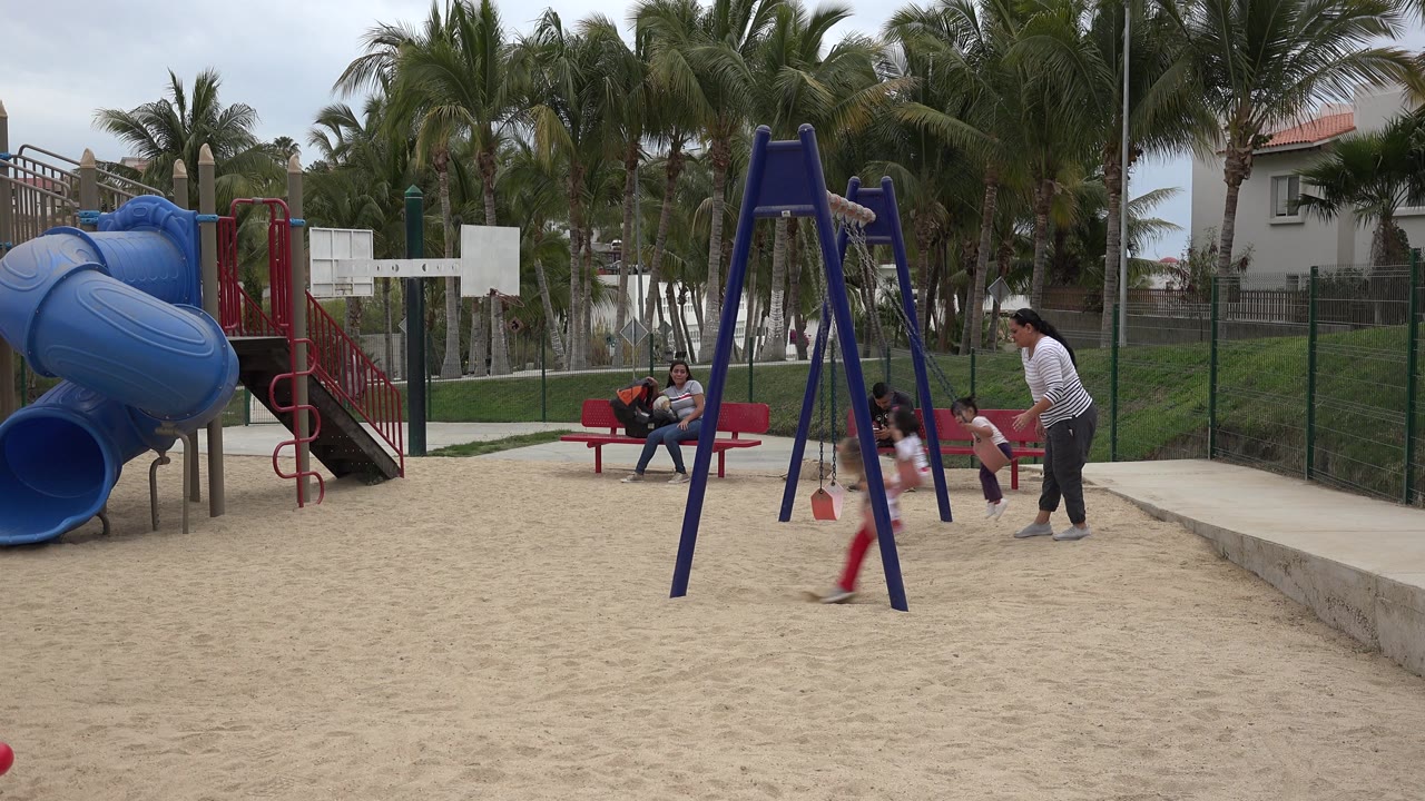 Child passes through the swing area while adults watch from the playground.