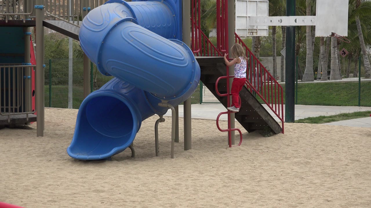 Girl climbs a red playground ladder beside a blue tube slide.