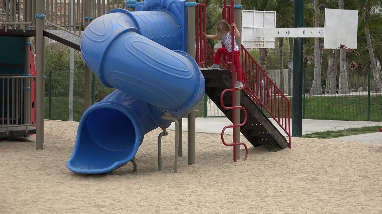 Child sits or crouches near the red ladder beside the blue slide.