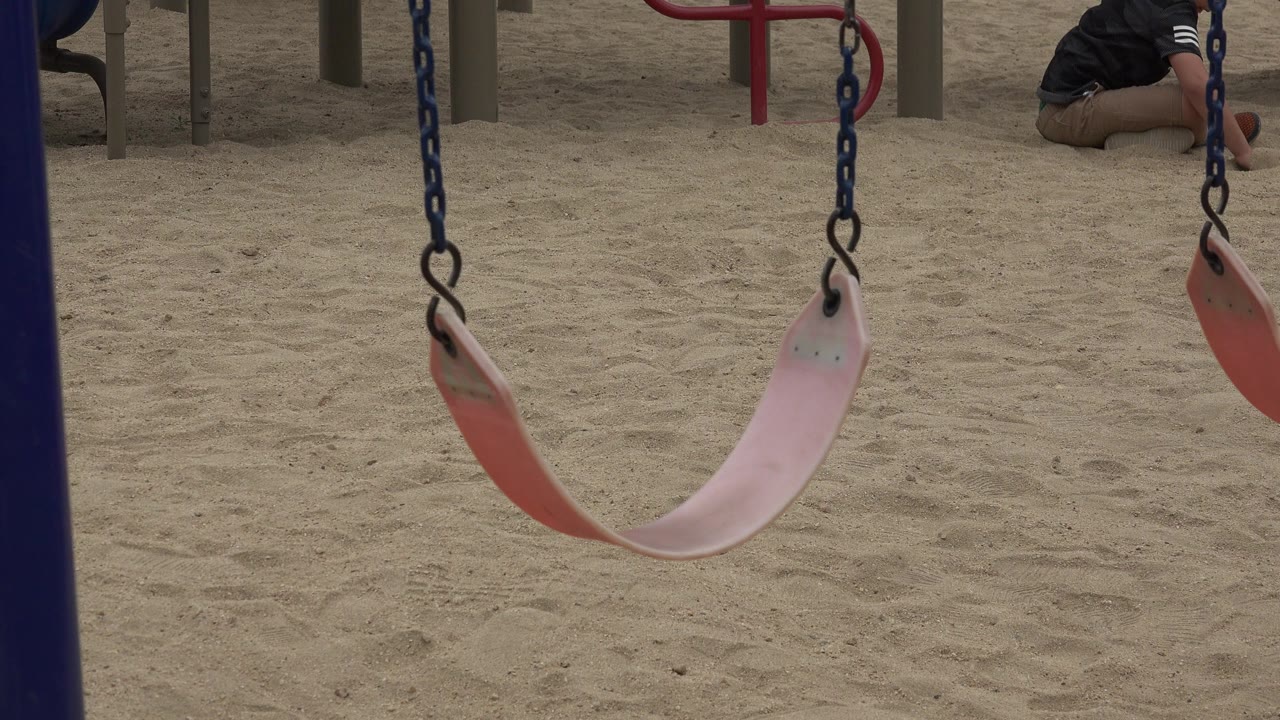 Pink and red playground swing hanging over sand.