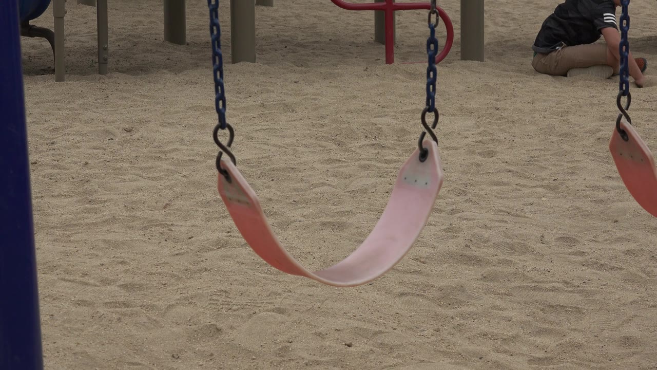 The belt swing sits centered over the sand in San Jose del Cabo, with vertical posts in back and a child partly visible near the top right of the frame.