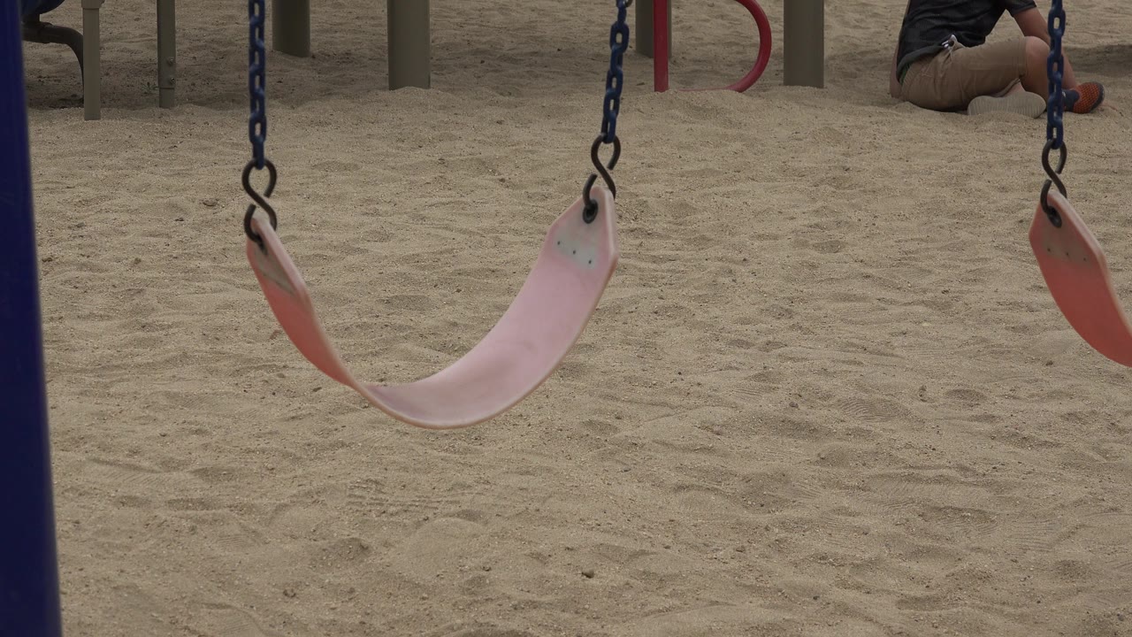 Empty pink swing hanging over sand with playground posts behind it.