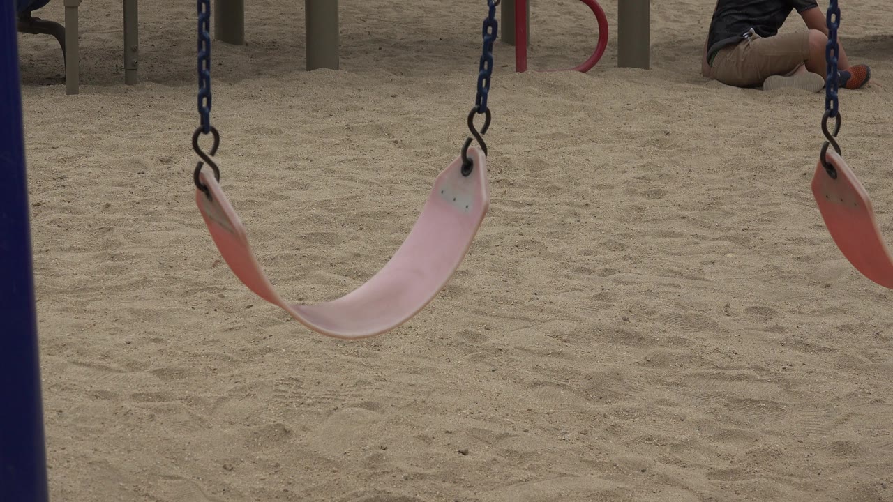 The swing remains centered over the sand in San Jose del Cabo, Mexico, with blue chains vertical and a cropped seated person still visible near the upper right background.