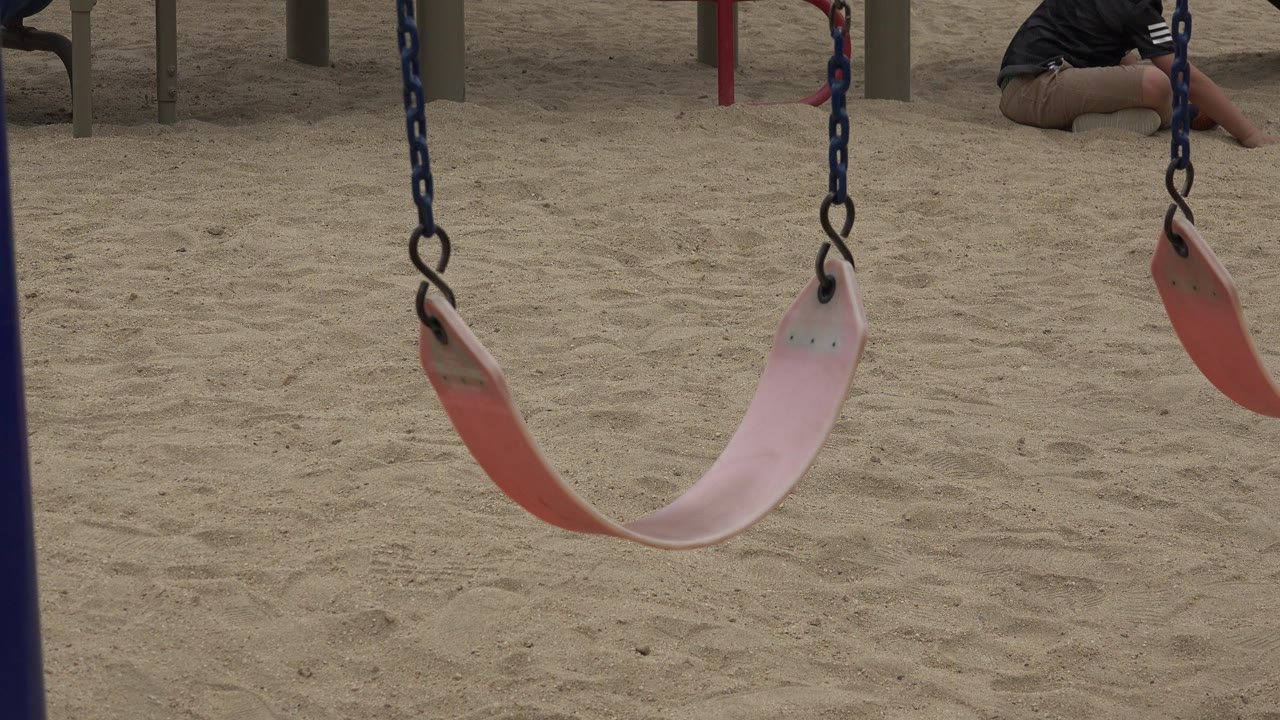 The empty swing remains near center over the sandy ground in San Jose del Cabo, with metal posts behind it and a partial person at the upper right edge.