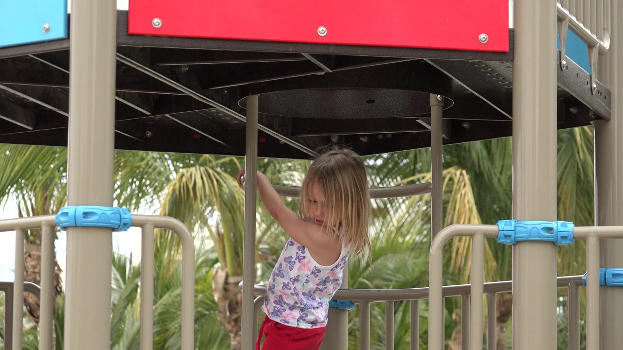 Young girl holding a playground rail under a red panel.