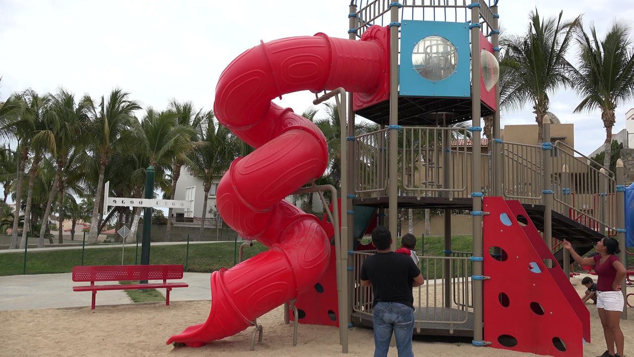 Red spiral playground slide with adults and children near the play structure.