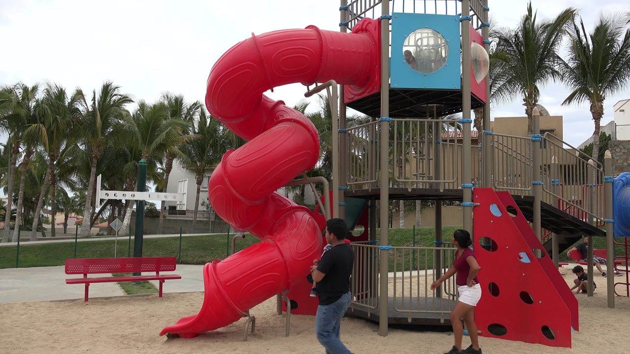 Parents and a child near a red playground slide.