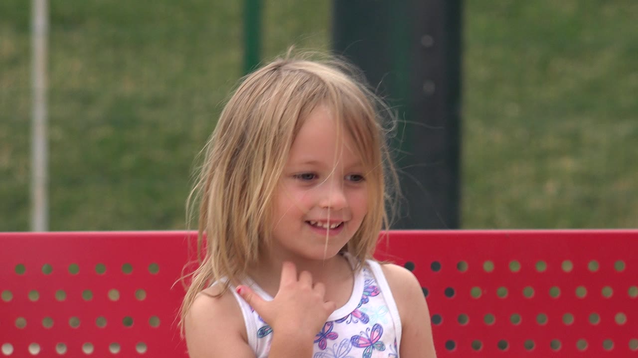 The child smiles while looking slightly down and to the side, with the red bench running behind her in San Jose del Cabo, Mexico.