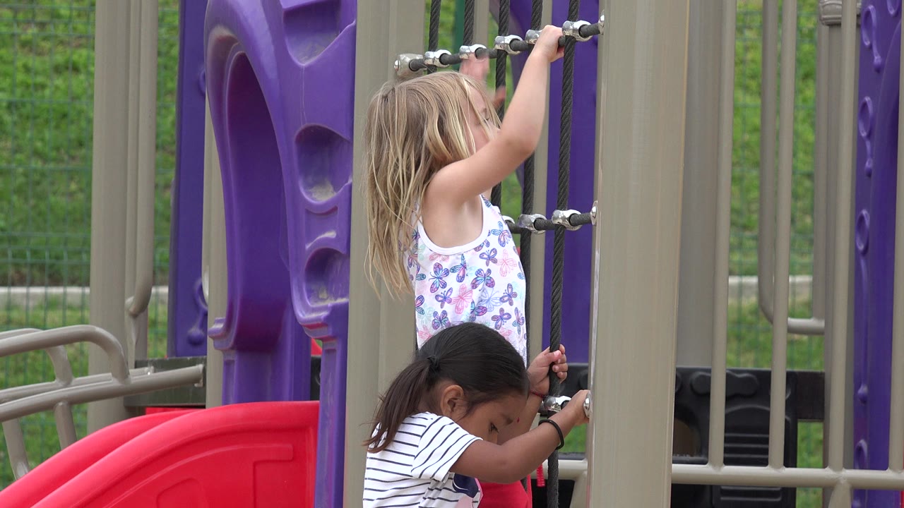 Two girls climbing rope playground equipment beside purple panels.