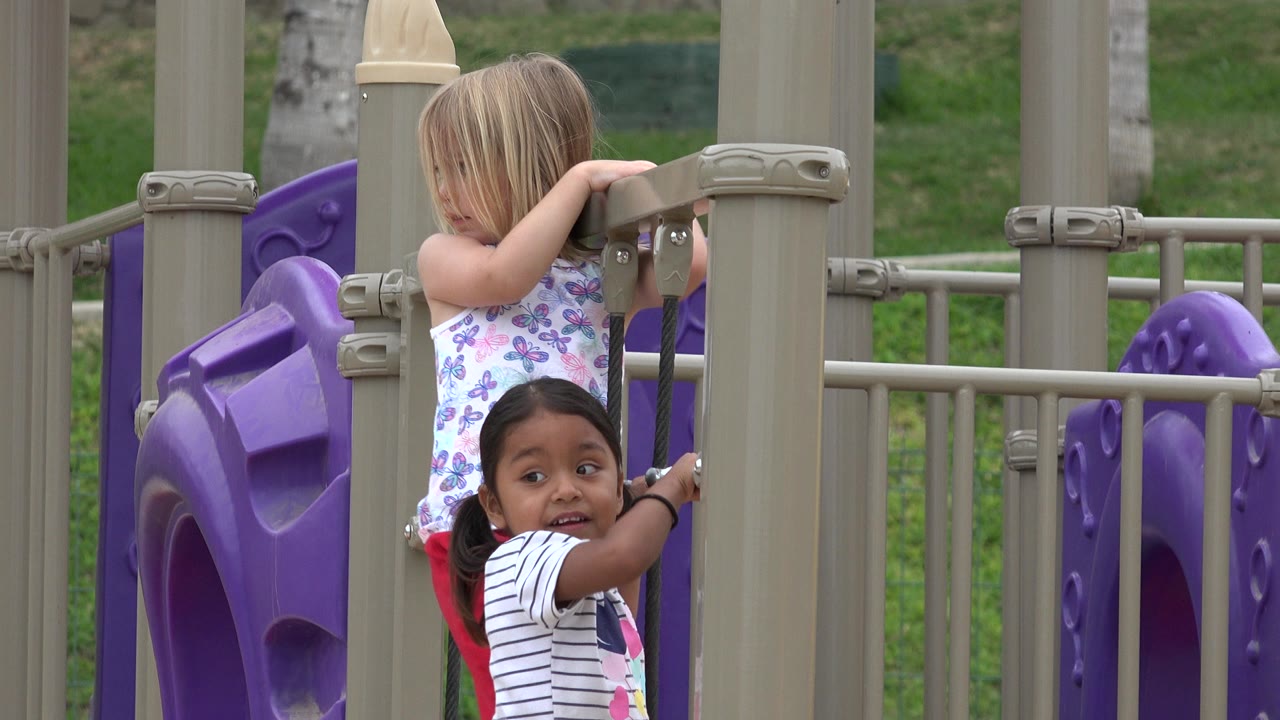 Two girls beside tan and purple playground equipment.