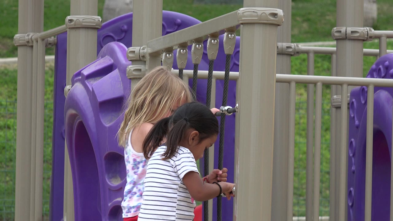 Two girls climbing on a playground rope net beside purple panels.