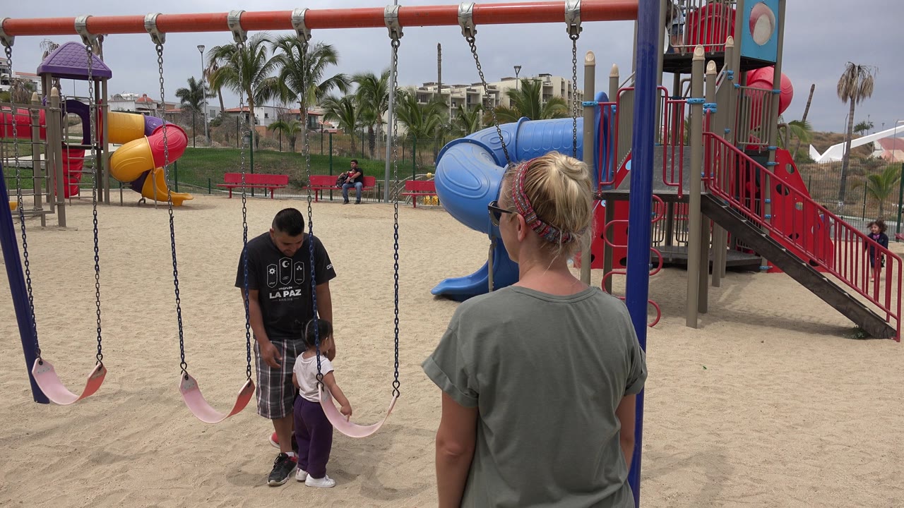 Adult man looks down toward a child beside a swing while another adult watches.