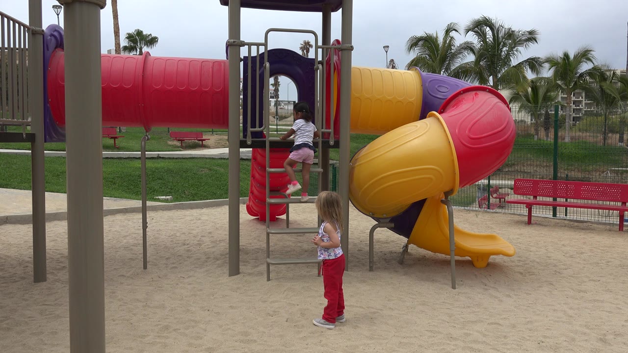 Two girls at a colorful playground with one climbing a ladder.