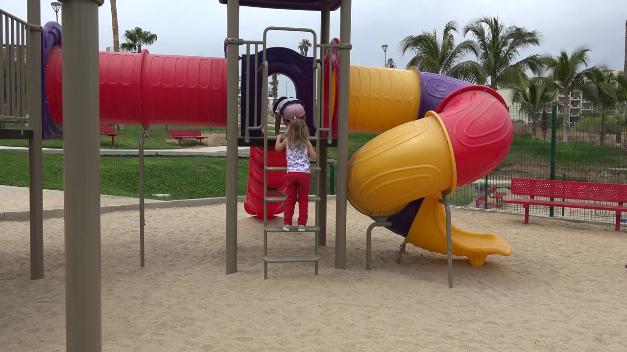 Child standing at a playground ladder beside a colorful tube slide.