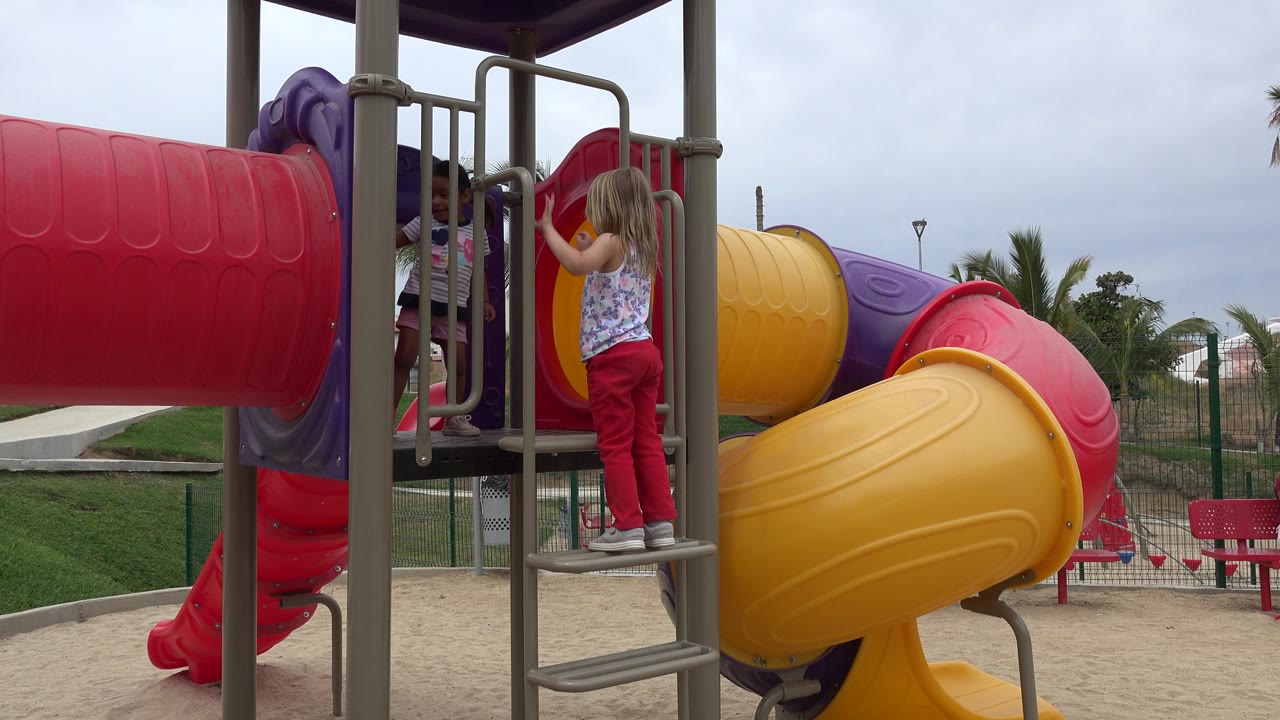 Girl reaches toward the playground rails while standing on the ladder.
