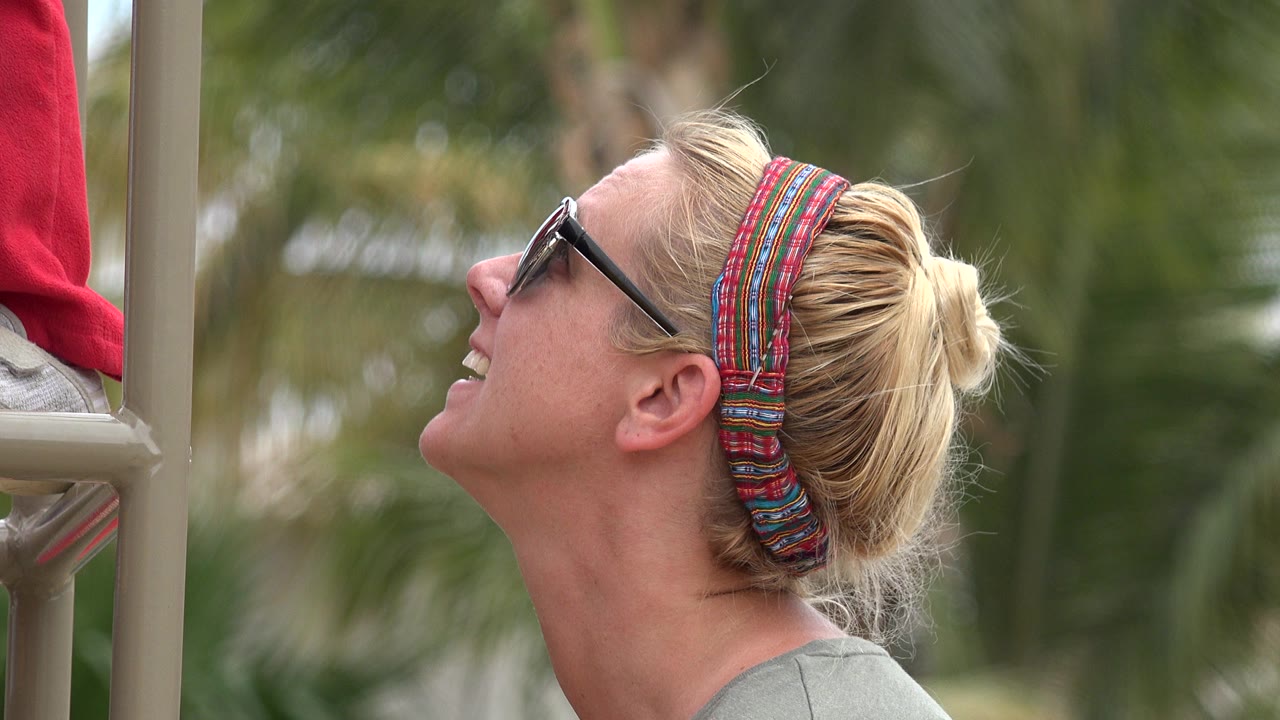 Blonde woman wearing black sunglasses and a red patterned head scarf smiles upward beside tan playground bars in San Jose Del Cabo, Mexico.