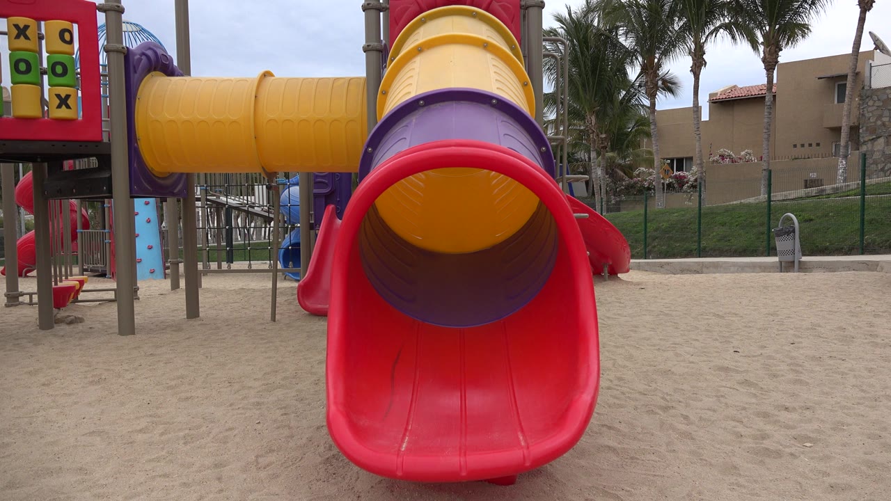Red playground slide under yellow and purple tube slide on sand.