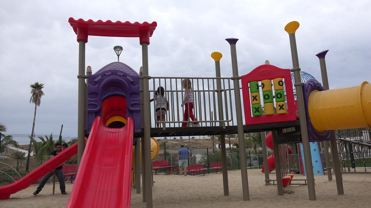 Two girls stand on a playground platform above a red slide.