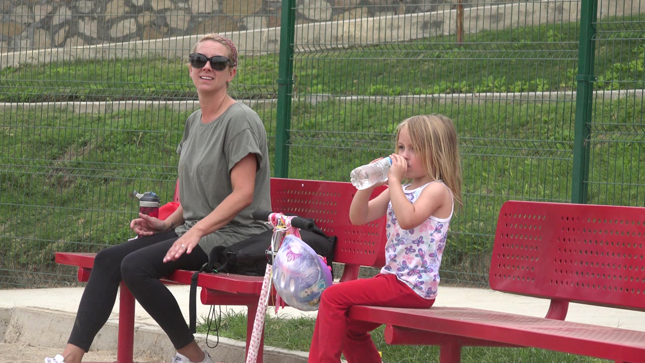 Woman and young girl sitting on a red bench beside a scooter.
