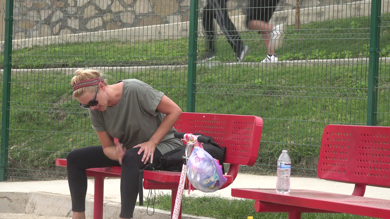In San Jose Del Cabo, Mexico, the seated woman looks down toward her lap on the red bench while the patterned bag and water bottle remain beside her.