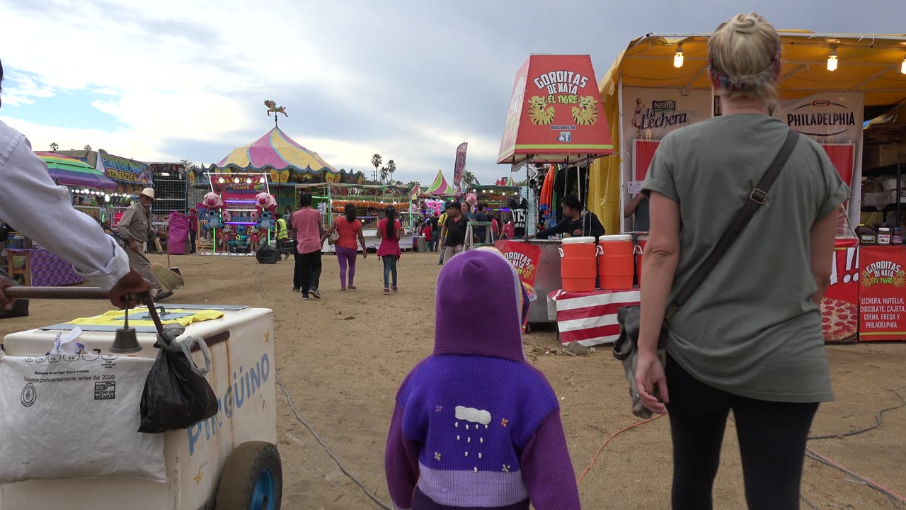Woman and child pass food stalls beside a fairground path.