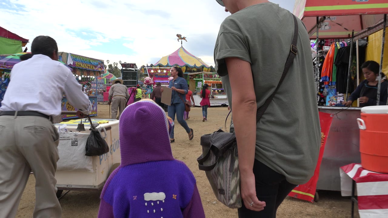 The child in purple and an adult in a green shirt continue along a dirt path while a man in a white shirt stands by a cart in San Jose Del Cabo, Mexico.
