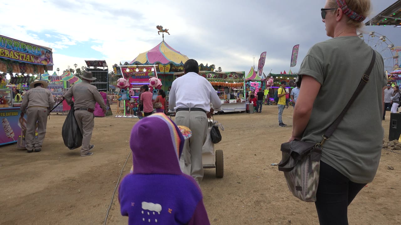 Uniformed workers carry bags as a child and adults face carnival attractions.