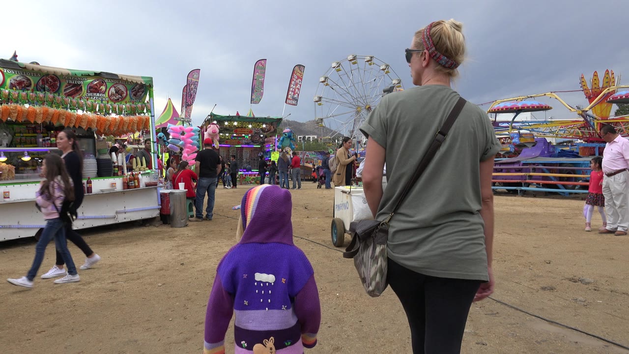 Mother and child walking toward carnival stalls and rides.