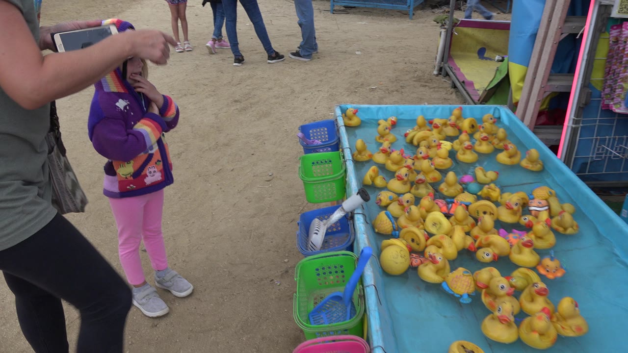Child and adult beside a blue rubber duck carnival game table.