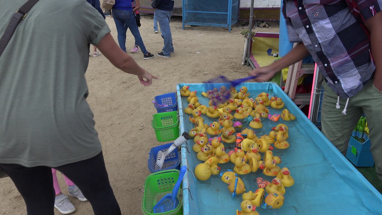 Adults standing beside a blue rubber duck game tank at a fair booth.