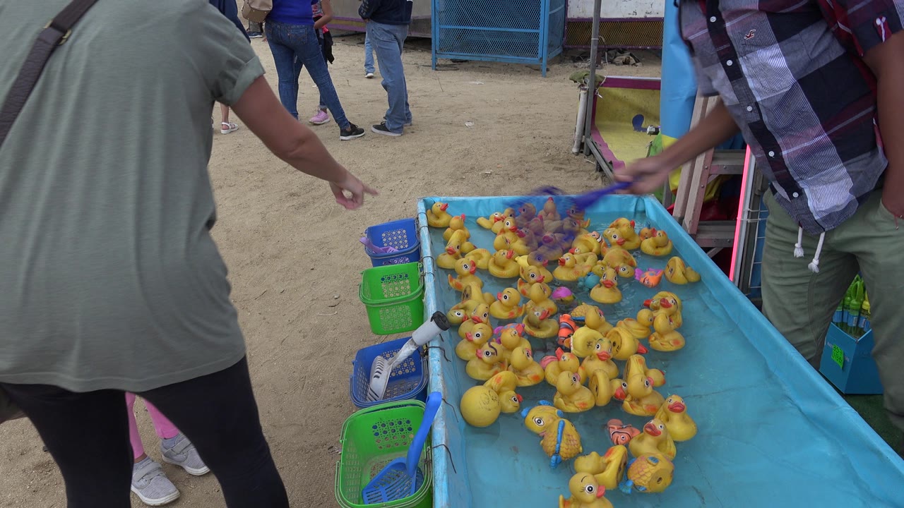 A hand moves over the crowded yellow rubber ducks in the blue tank as adults stand around the San Jose del Cabo game booth.