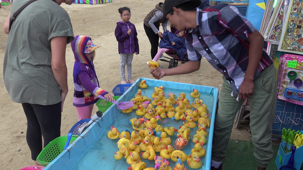 Child reaches toward a blue duck fishing game with adults nearby.
