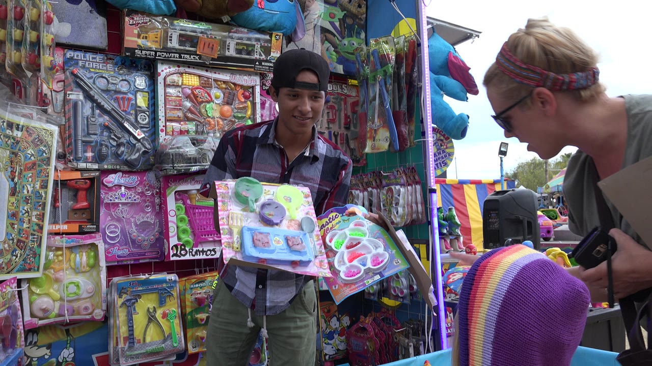 Prize booth attendant holding toy packages beside a woman and child at a duck game.