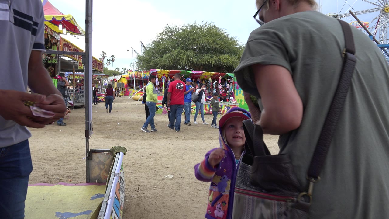 Child in purple hoodie beside adults at an outdoor carnival game.