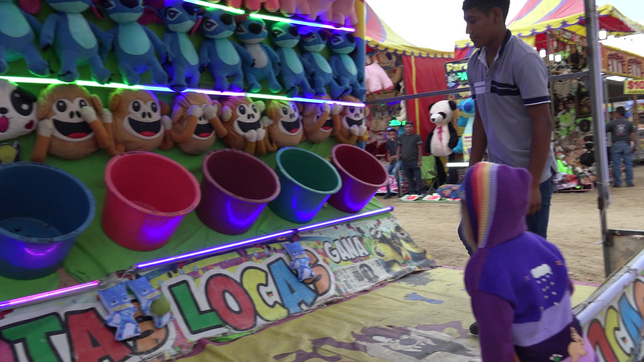 Child in a purple hoodie faces a carnival bucket game booth.