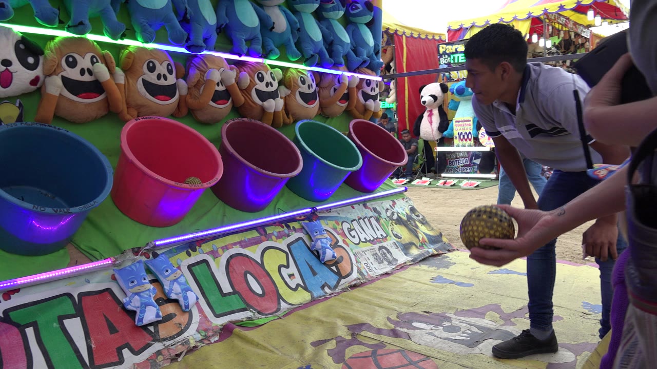 Carnival ball toss booth with plush prizes, buckets, and a booth attendant leaning in.