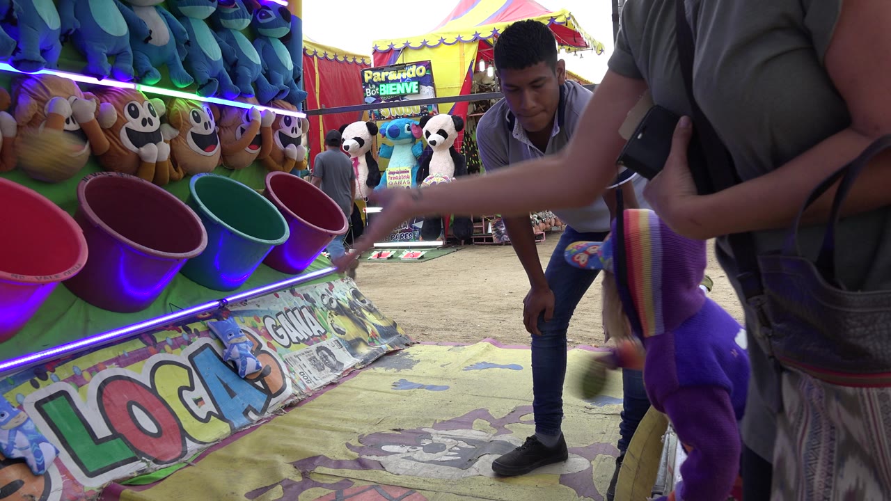 Adult throws a ball toward carnival game buckets as attendant stands nearby.