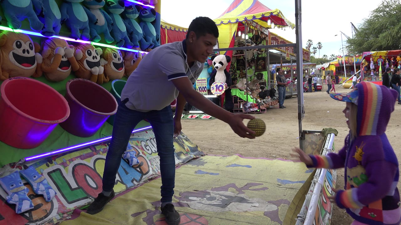 Adult man reaches toward a child at a colorful ball toss booth.