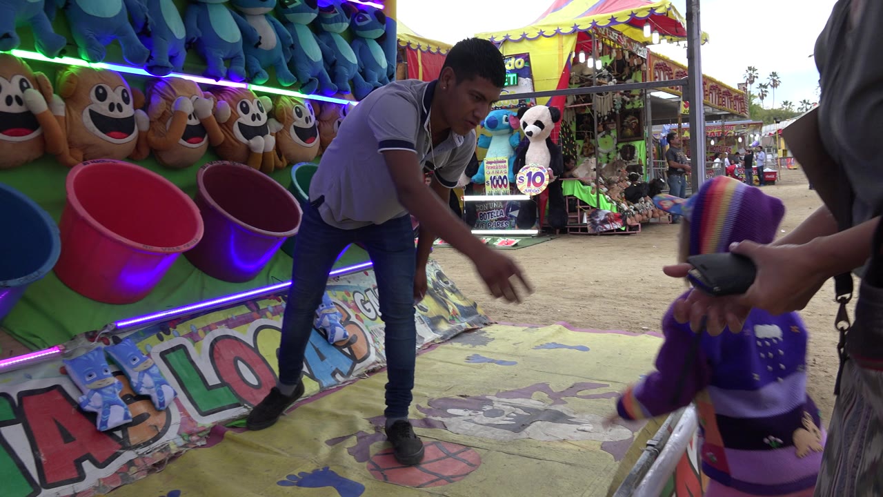 In San Jose del Cabo, Mexico, the adult remains bent toward the game while the child turns at the right edge, and the prize booth fills the left side of the frame.