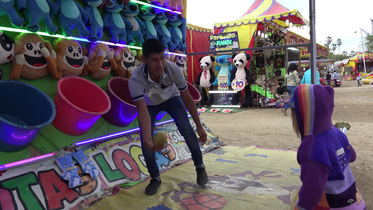 Attendant holds a small ball near a child at a colorful fair game booth.