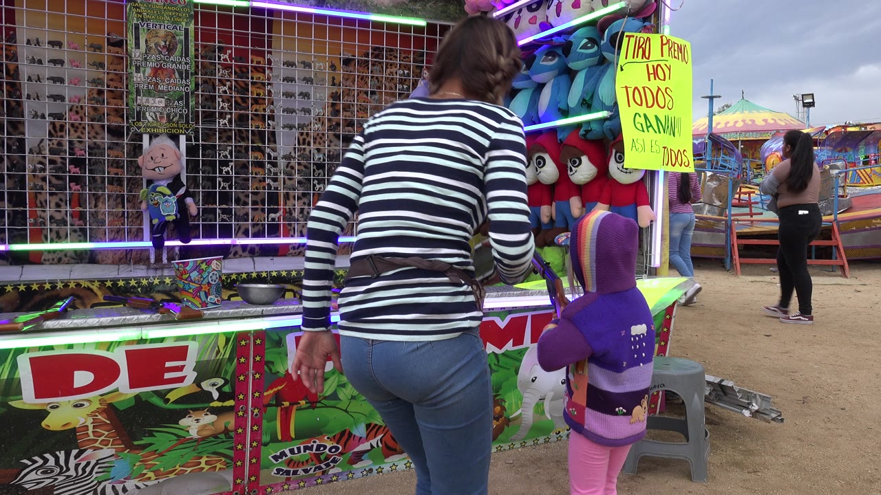The woman stands closer to the carnival game counter while the child in purple remains beside the prize display in San Jose Del Cabo, Mexico.