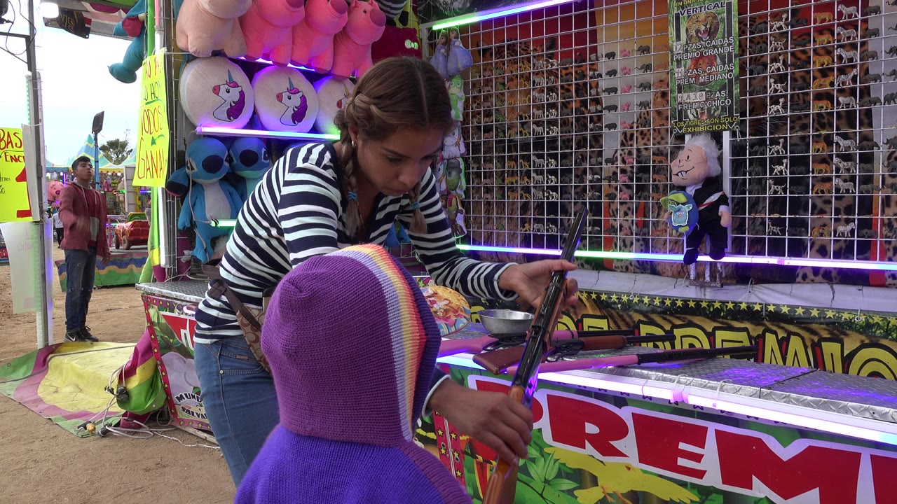 Child holds a toy rifle while an adult adjusts it at the booth.