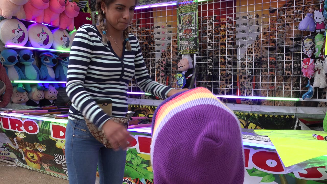 Girl in purple hood facing a carnival game attendant at a prize booth.