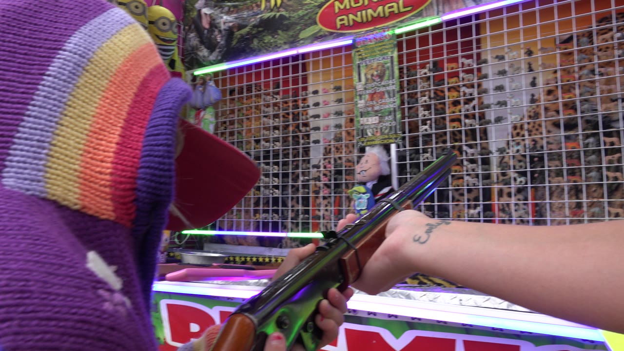 The San Jose del Cabo shooting gallery remains framed over the child's shoulder as adult hands help steady the gun toward the prize grid.