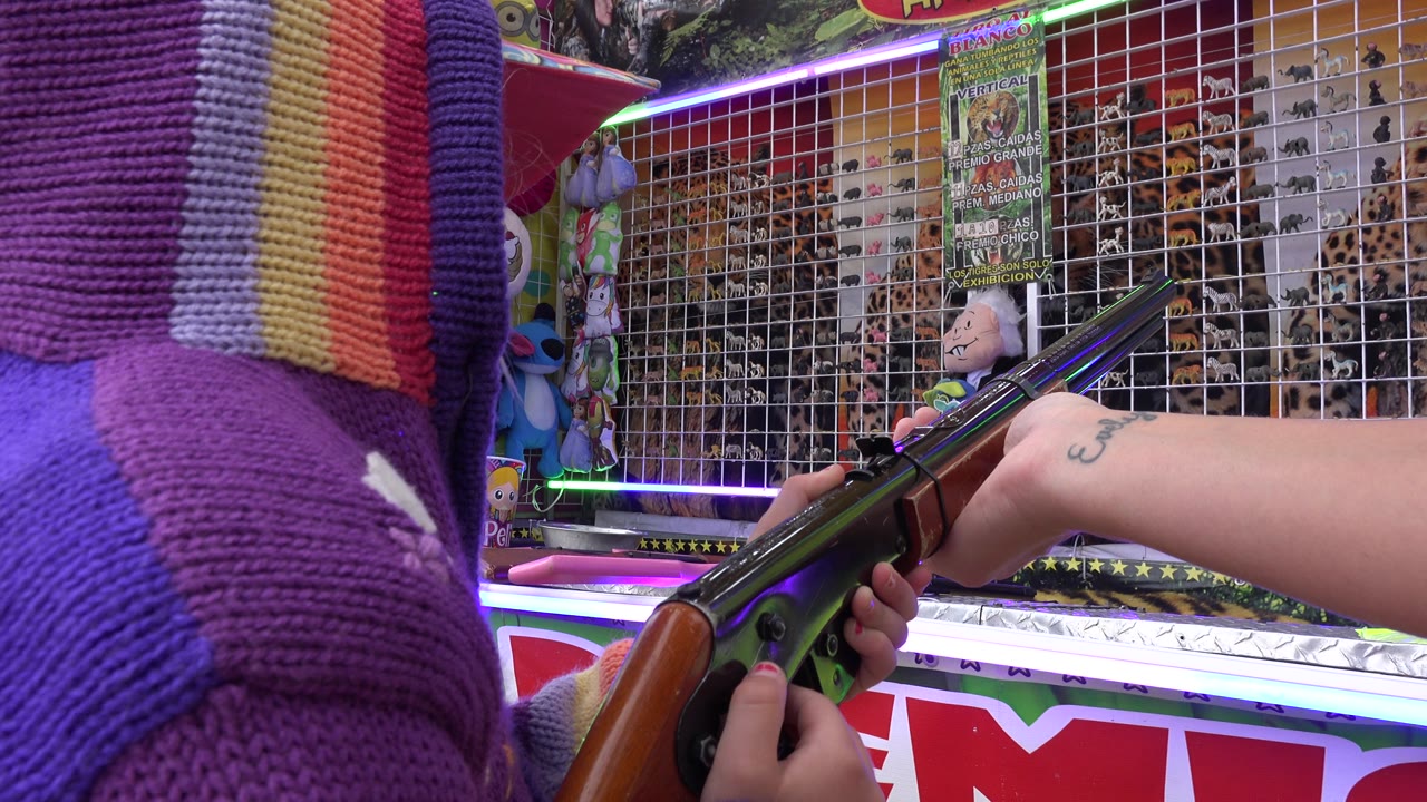 Carnival gun angled toward a gridded wall of hanging prizes.