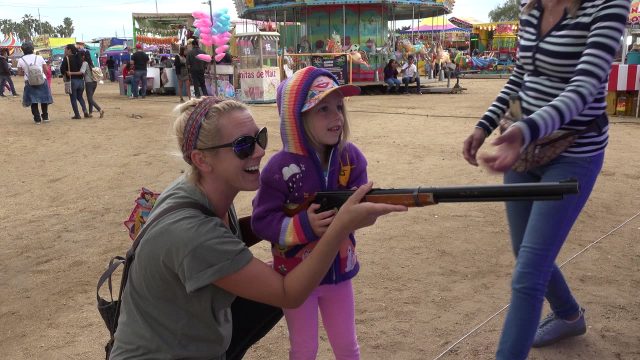 Adult woman and young girl holding a toy rifle at a fairground game.