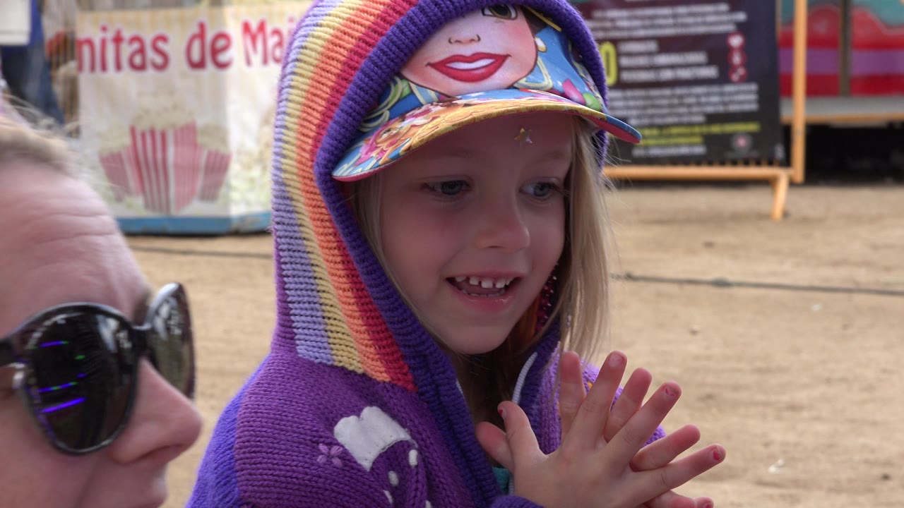 The child in a rainbow knit hat looks downward while an adult woman in sunglasses remains close beside her in San Jose del Cabo.