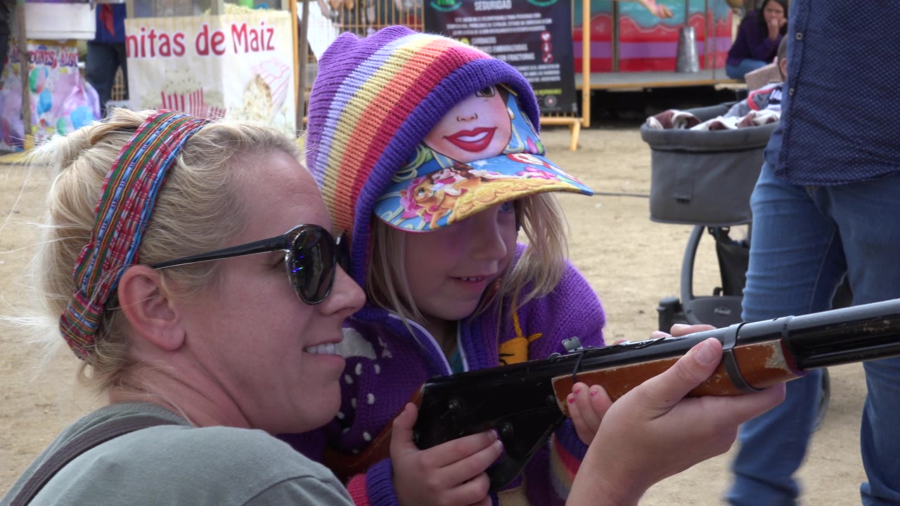 Mother and child holding a toy rifle outdoors.