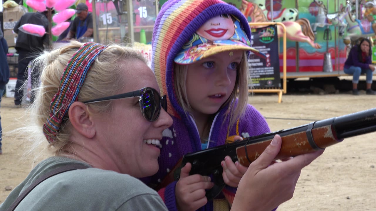 Adult woman and young girl holding a toy rifle at a fairground.